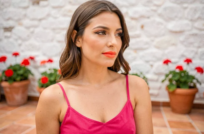 Femme en robe fuchsia avec un rouge à lèvres corail vif et un regard naturel en extérieur