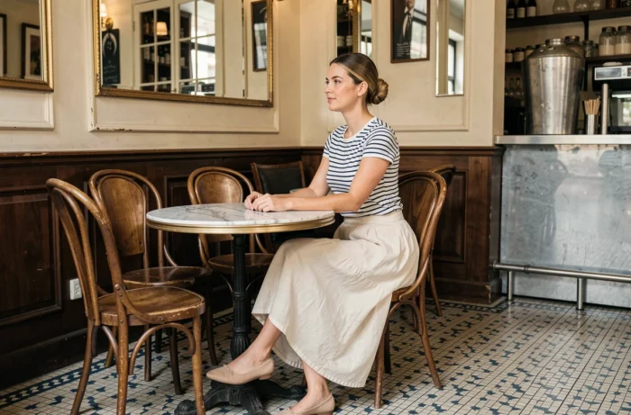 Femme chic en marinière rayée et jupe en lin assise dans un café parisien au décor vintage